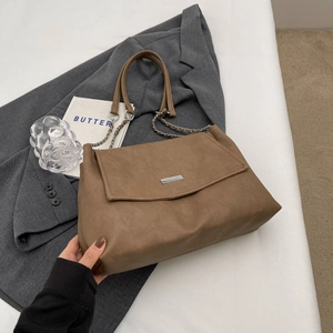 Detailed view of brown matte leather bag with silver logo plaque on gray blazer