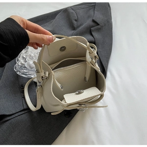 Detail der cremefarbenen Leder-Beuteltasche mit silbernen Beschlägen auf grauem Blazer