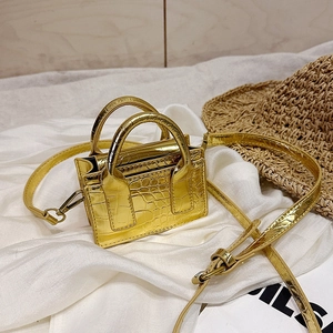Mini gold crocodile texture crossbody bag with top handles on white fabric background
