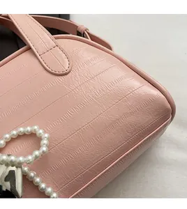 Gros plan du sac à main rose montrant le motif crocodile brillant et la sangle en perles