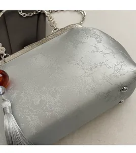 Detail of silver-grey jacquard evening bag with floral patterns and luxury tassels