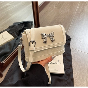 Detail of cream crossbody bag featuring glossy crinkled texture and silver butterfly buckle