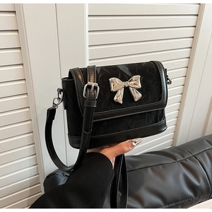 Detail of a black mini crossbody bag featuring a large silver metal bow decoration