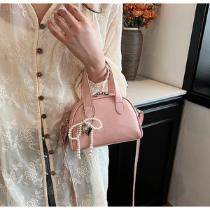 Sac rose en similicuir avec texture crocodile et détail perle tenu par un mannequin