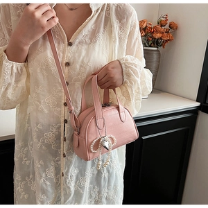 Détail du sac bandoulière en cuir rose avec pendentif nœud en perles et charme cœur