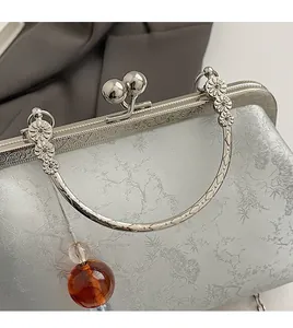 Detail of silver floral jacquard fabric and carved metal handle with amber bead charm
