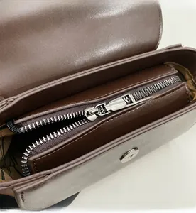 Detail of dark brown leather handbag featuring a smooth silver zipper and magnetic buckle
