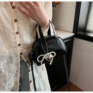 Détail du sac noir à texture crocodile avec nœud en perles et pendentif cœur en métal
