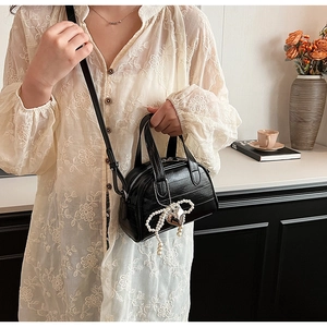 Détail d'un sac à main noir brillant avec nœud en perles et breloque cœur en situation réelle