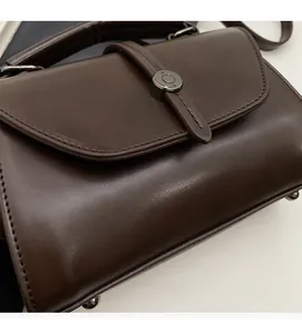 Detail of dark brown retro square bag showing soft glossy leather and metal buckle