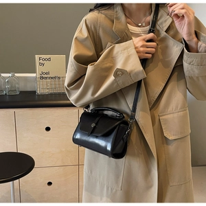 Detail of a black leather square handbag with silver buckle and crossbody strap on a model