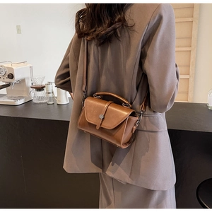 Close-up of a vintage brown crossbody bag with metal buckle in a cozy cafe setting
