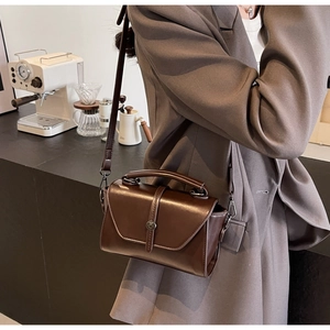 Detail of dark brown leather handbag with metallic buckle shown in a warm cafe setting