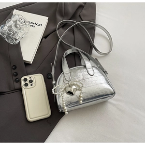 Détail d'un sac à main argenté métallisé avec nœud en perles sur fond de blazer gris
