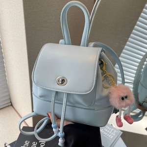 Mini zaino celeste con chiusura argentata e ciondolo di peluche rosa in un contesto di moda