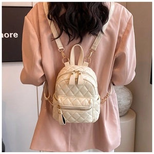 Elegant white quilted mini backpack with golden zippers shown on model in casual suit