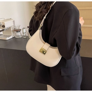 Détail du sac demi-lune crème avec fermoir doré dans un décor urbain moderne