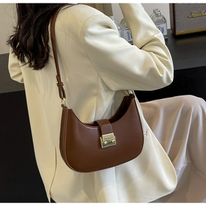 Détail d'un sac selle marron en forme de demi-lune avec boucle en métal doré et fini lisse