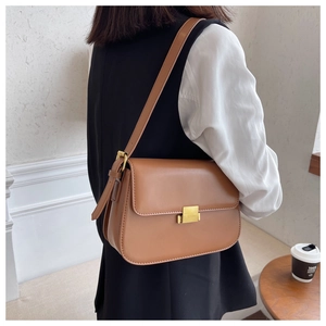 Brown leather crossbody bag detail with golden square lock on a stylish casual outfit