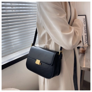 Detail of a black minimalist box bag with gold buckle on a model wearing a white coat