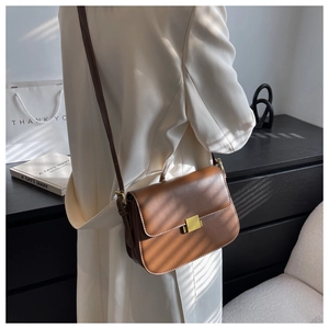 Brown leather crossbody bag with gold metal buckle shown on a model in urban style