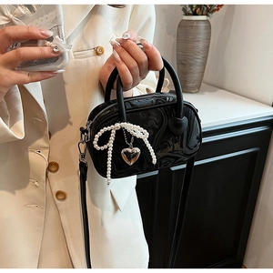 Detail of black marble textured velvet handbag with pearl bow and heart charm