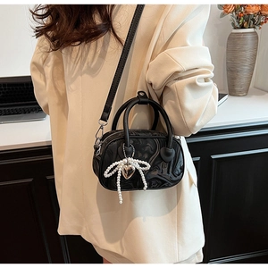 Detail of black glossy Boston bag with pearl bow charm on a model in beige blazer