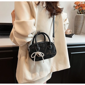 Detail of black marble textured bag with pearl bow charm worn with a cream blazer