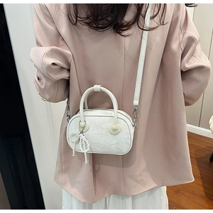 Detail view of white marble patterned handbag with pearl bow charm on a model