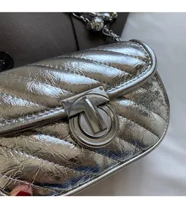 Close-up of silver quilted chain bag featuring large metallic T-shaped twist lock closure
