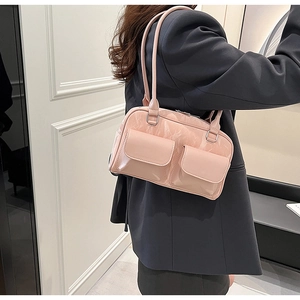 Close-up of pink patent leather shoulder bag with dual front pockets on grey blazer