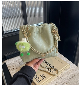Detail of green bucket bag with pleated texture and gold chain strap and plush charm