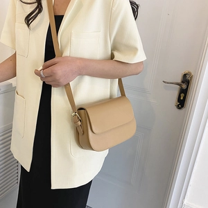 Detail van een lichtbruine leren crossbodytas met minimalistische flap op een model