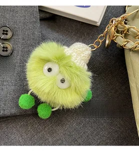 Detailed view of a fuzzy green monster bag charm with a knit hat on a stylish handbag