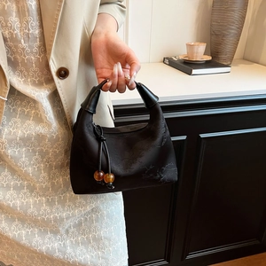 Detail of black satin dumpling bag featuring bamboo embroidery and amber bead accents