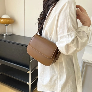 Detail van een bruine mat lederen crossbody tas met verstelbare riem gedragen door model