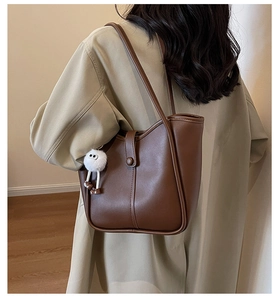Detail of deep brown leather tote bag with white plush charm worn with a trench coat