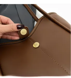 Close-up of golden magnetic cylindrical clasp and brown textured leather tote bag detail