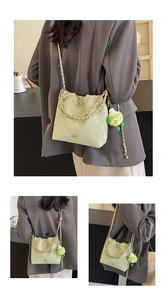 Detail view of light green pleated bucket bag with metal text and plush monster charm