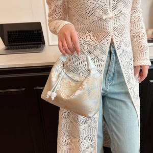 Detail of light blue satin dumplings bag with gold embroidery and white pearl tassels
