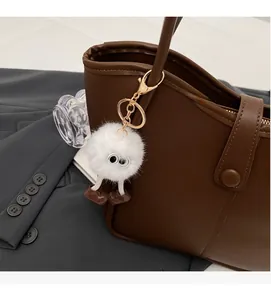 Close-up of white fur monster charm with boots accessory on a brown bucket bag