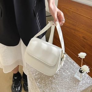 Minimalistische witte lederen crossbodytas op een helder voetstuk met bloemendecor