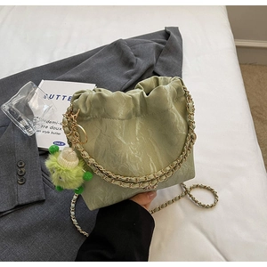 Detail of light green cloud bag with gold chain and plush monster charm on bedding