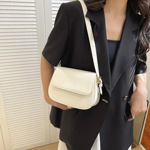 Detail van een witte lederen zadeltas met gouden gesp op een model in zwarte blazer