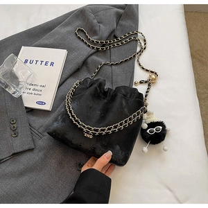 Detail of black velvet bucket bag with chain strap and cute monster plush pendant