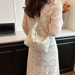 Detailed embroidery of birds and flowers on a satin dumpling bag with pearl drawstring