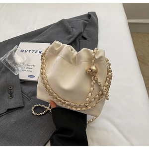 Close-up of cream drawstring bucket bag with gold chain and spherical metal buckle