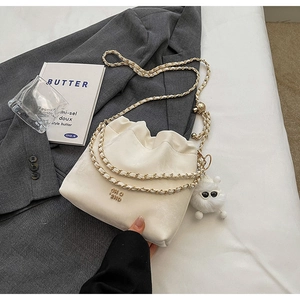 Close-up of cream bucket bag with gold chain strap and a cute white plush toy charm