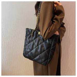 Close-up of black quilted leather tote bag with gold chain strap and metal lock detail