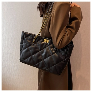 Detail of a large black quilted tote bag with chain strap worn with a blazer